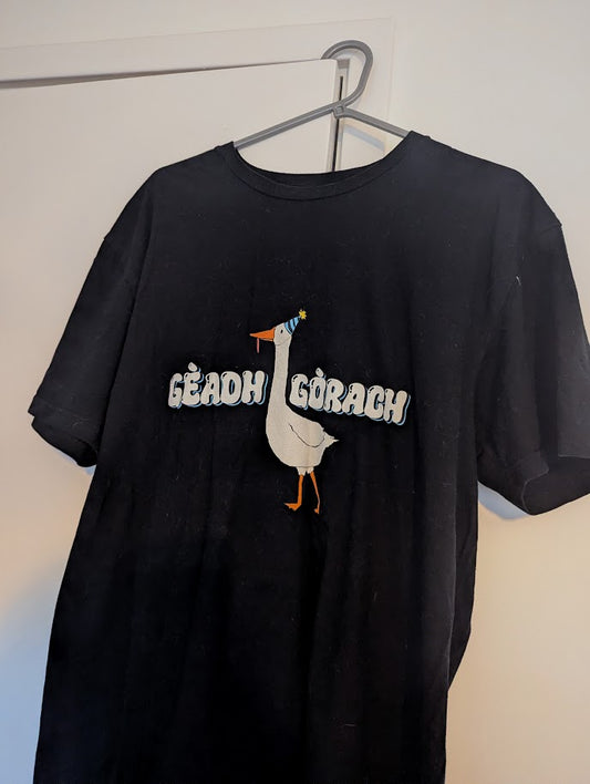 Black t-shirt with a graphic design of a goose and text on a hanger against a white wall.